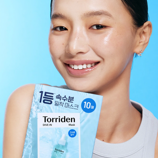 A smiling woman in a white top holds a package of Torriden Dive In Mask against a bright blue background.