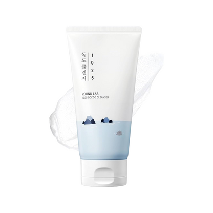 A white squeeze tube of Bound Lab 1025 Korean Cleanser with a light blue lower section and small mountain illustrations, shown on a clean white background with a faint translucent wave graphic behind it.