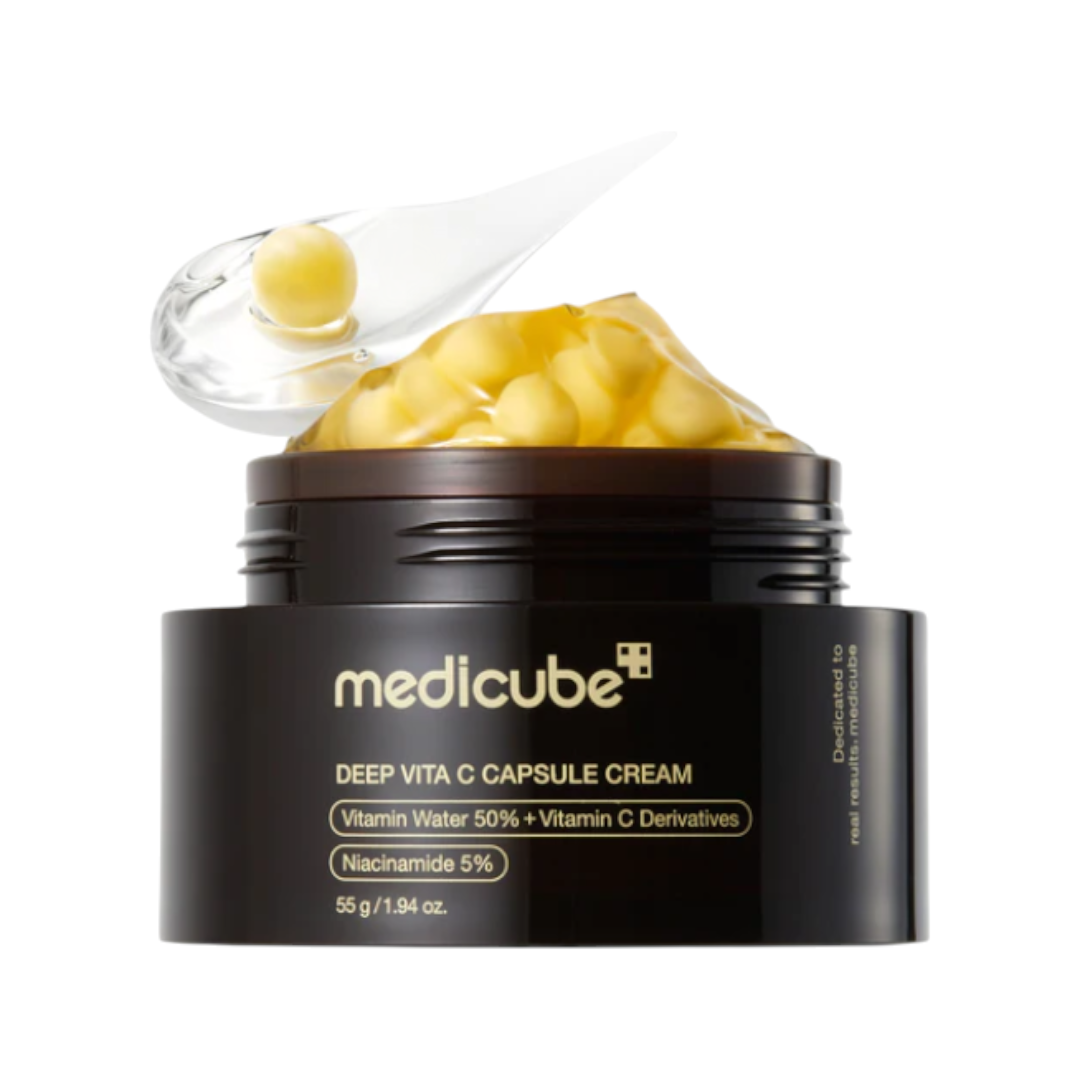 A jar of medicube Deep Vita C Capsule Cream with the lid open, showing yellow gel capsules inside and a clear scoop with a capsule on top, set against a plain white background.