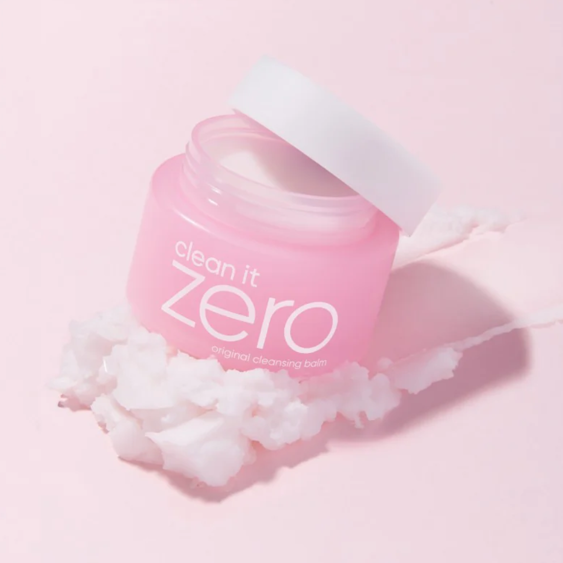 Pink jar of Clean It Zero Exfoliating Cleansing Balm with white lid, shown on a pink background with white exfoliating balm residue.