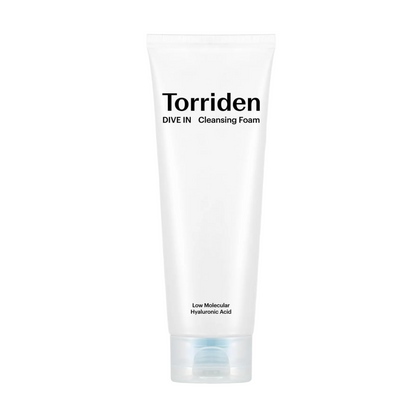 A white tube of Torriden Dive In Cleansing Foam centered on a white background with a large dollop of white foam behind it. The tube has black text reading 'Torriden' and 'DIVE IN Cleansing Foam' with smaller text near the bottom.