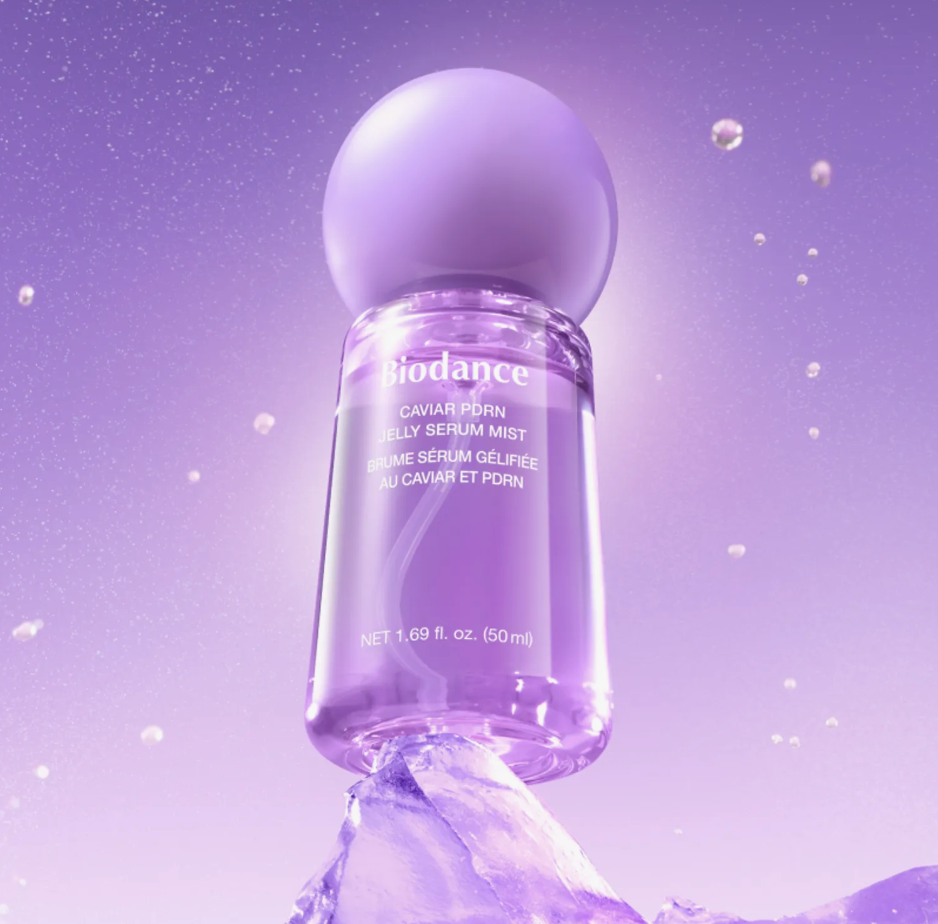 Biodance Caviar Porn Jelly Serum Mist in a clear cylindrical bottle with a rounded lavender-purple cap, shown on a purple gradient background with floating droplets and a stylized purple base.