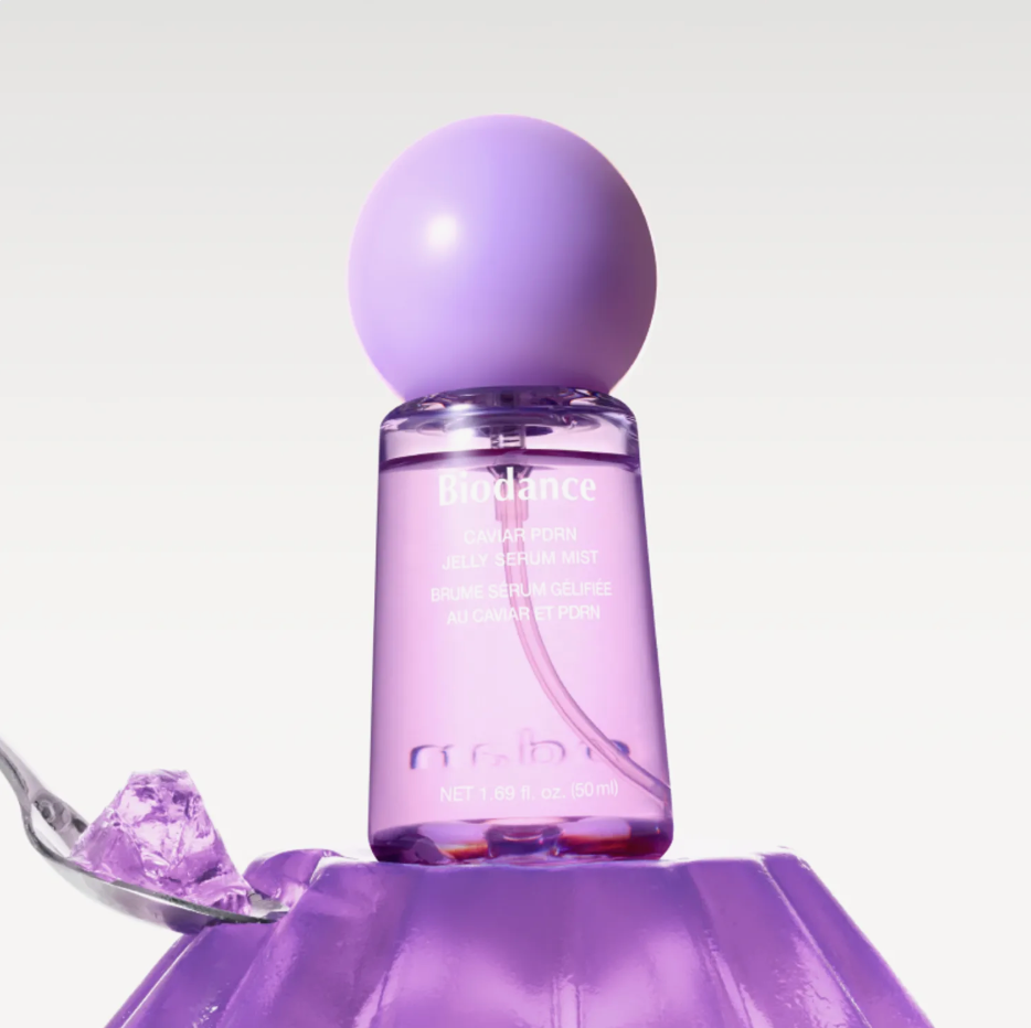 Biodance 109 Calming Aromatic Mist in a clear cylindrical bottle with a matte lavender-purple spherical cap, shown on a white background with a spoonful of purple gel and ice in the foreground.