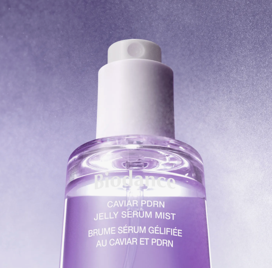 Biodance Caviar PDRN Jelly Sérum Mist in a clear bottle with a white pump dispenser, showing a purple liquid inside, set against a textured purple background.