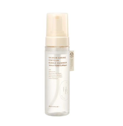 A bottle of Salmon Caring Centella Bubble Cleanser by L'Artisan du Bégumel, featuring a clear cylindrical bottle with a beige pump dispenser and a small beige tag, set against a light gray background.