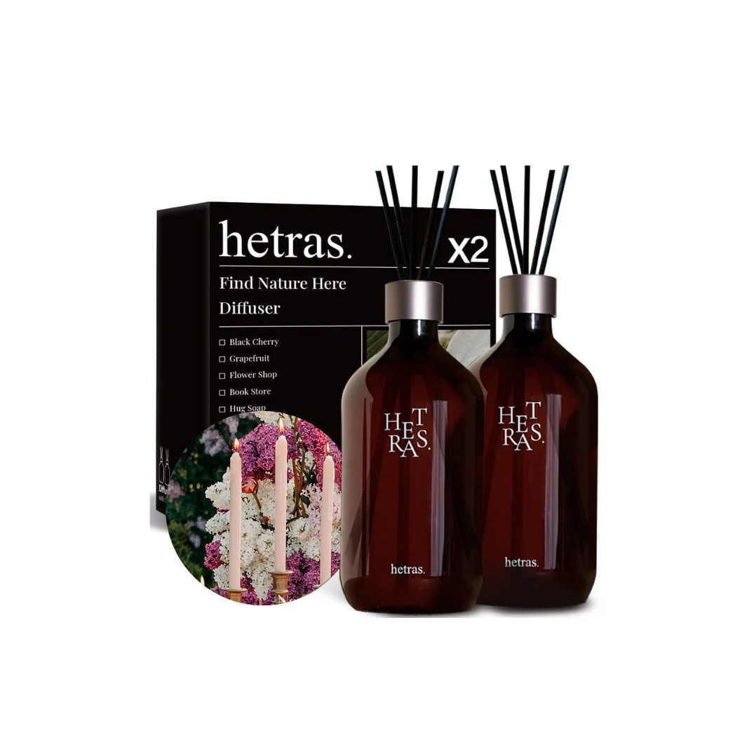 Two Hetras diffuser bottles with dark amber glass and black reeds, shown in front of a black product box with a floral illustration. The Hetras brand name is visible on both the bottles and the box.