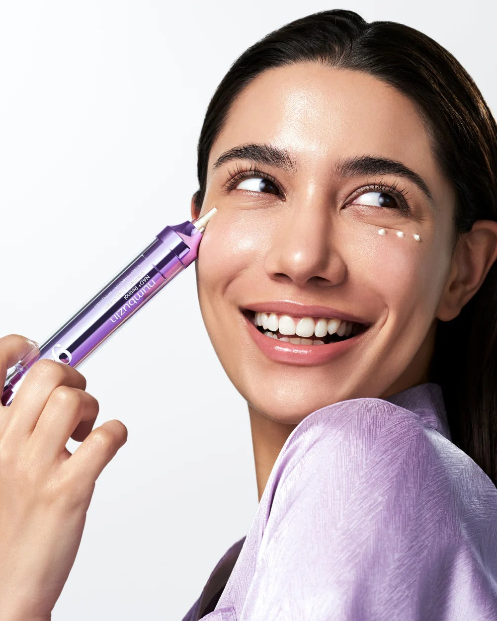 Woman applying a purple cosmetic device to her face against a white background