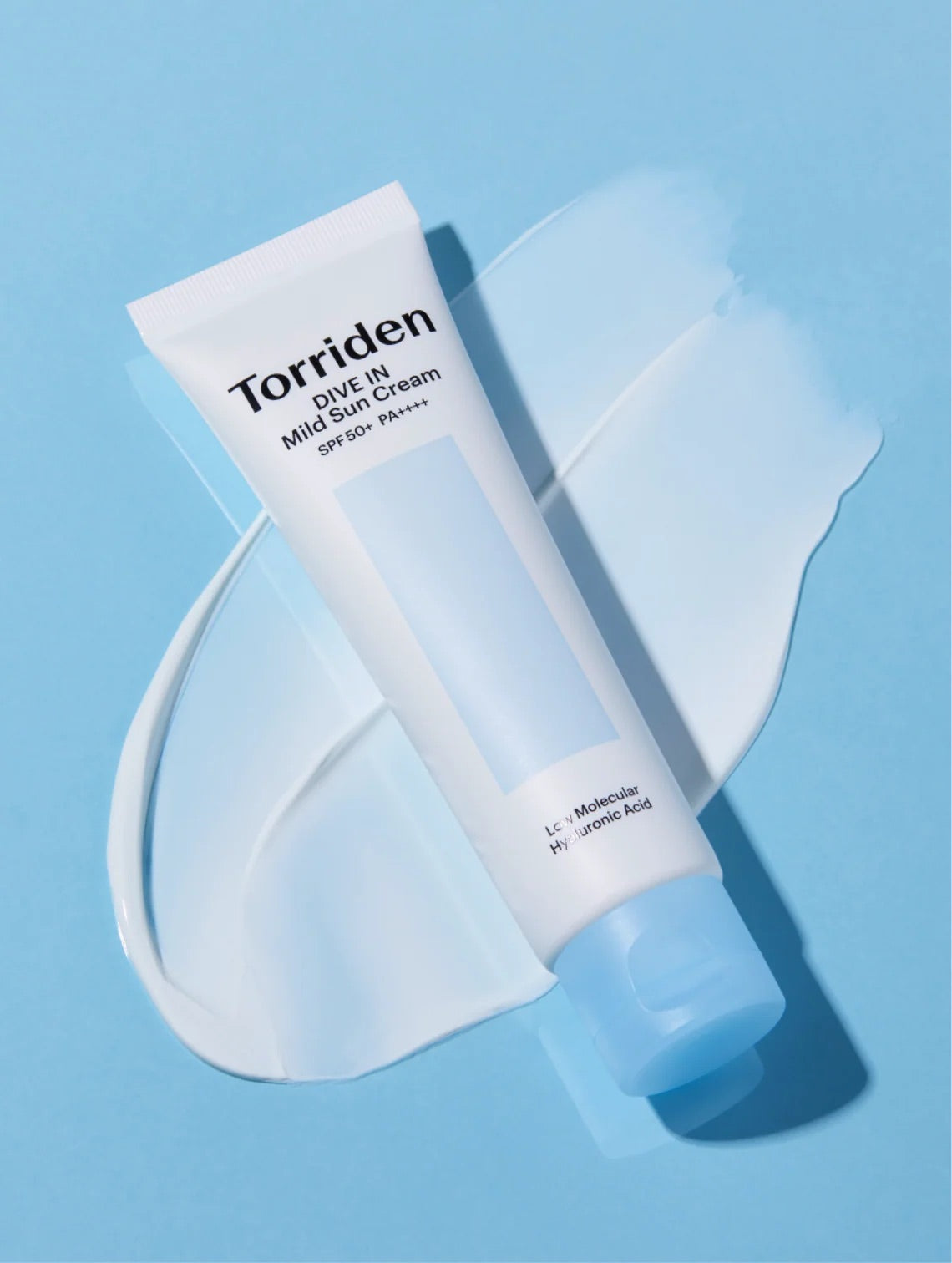 A tube of Torriden Dive In Mild Sun Cream SPF 50+ lies diagonally on a light blue background with a white cream smear behind it.